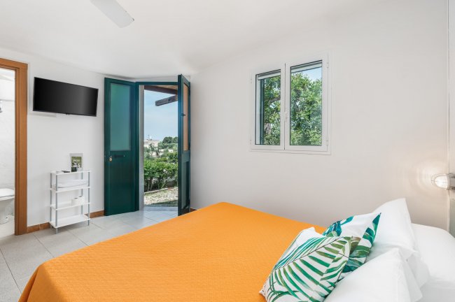 Camera con letto arancione e porta finestra con vista giardino.