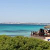 Spiaggia con mare azzurro e chiosco con tetto di paglia.