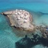 Piccola isola rocciosa con ombrelloni e lettini in un mare cristallino.