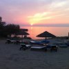 Spiaggia al tramonto con ombrelloni e lettini, cielo rosa e mare calmo.