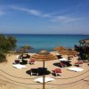 Spiaggia con ombrelloni di paglia, lettini rossi e bianchi, mare blu sullo sfondo.