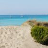 Dune di sabbia con mare e barche lontane.