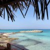 Spiaggia con acqua cristallina e cielo blu, vista da un tetto di paglia.