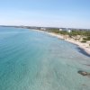 Spiaggia lunga con acqua turchese e edifici in lontananza.